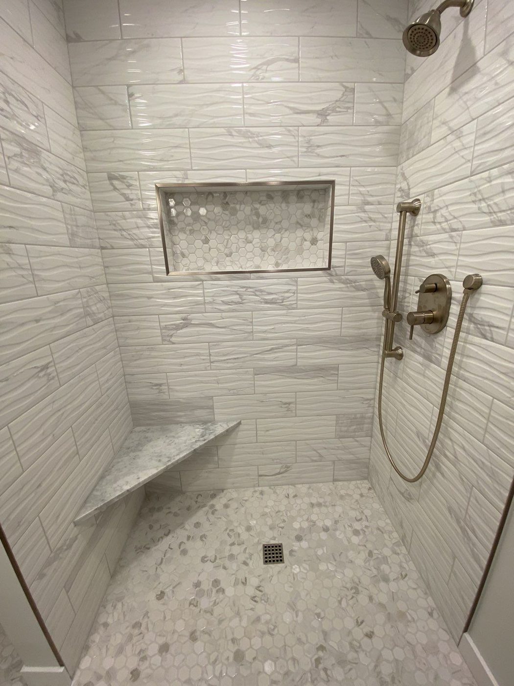 Walk-in shower with white linear tile, marble corner bench, and tile niche