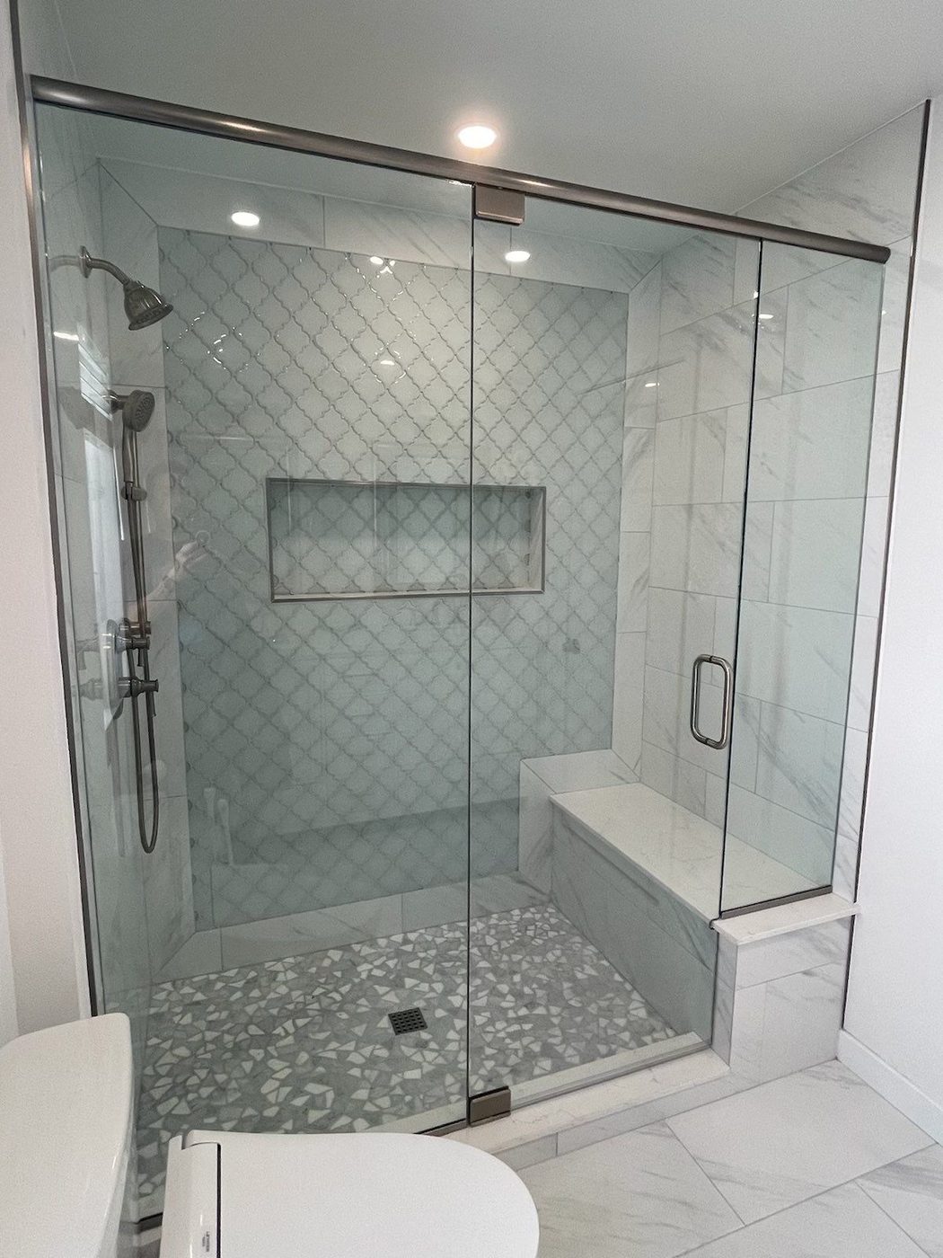 Glass-enclosed shower with arabesque tile, pebble floor, and marble bench
