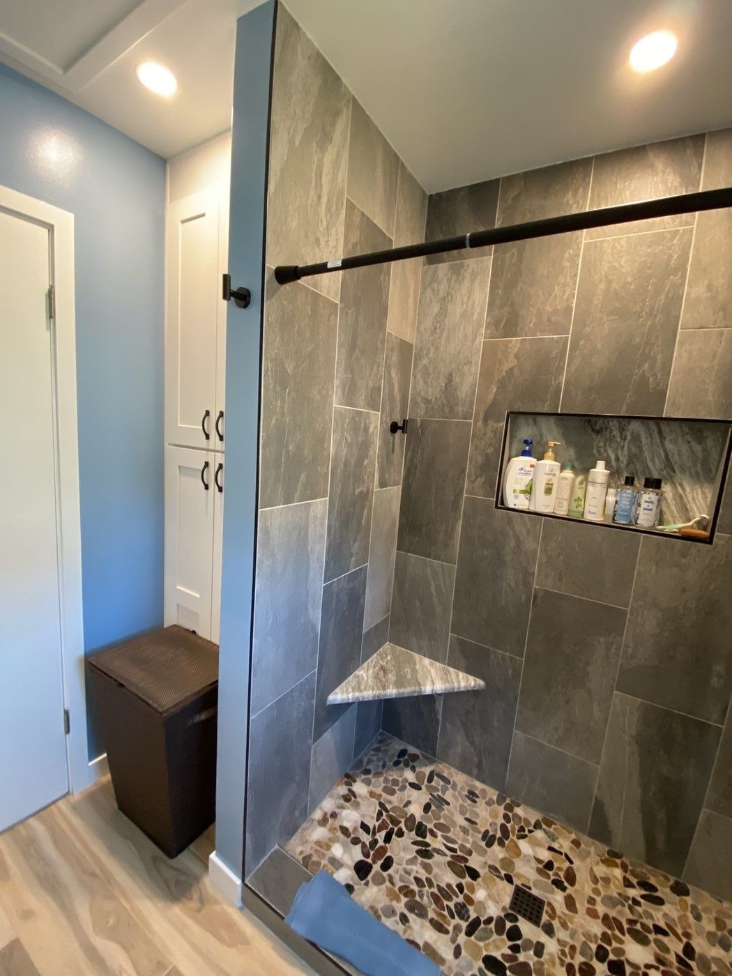 Slate walk-in shower with river rock floor and wood-look flooring