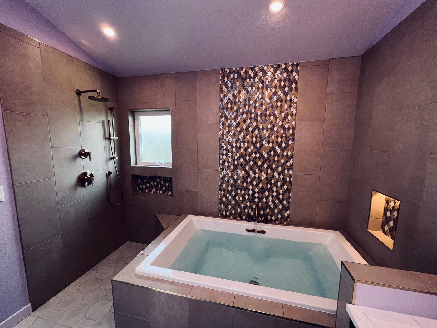 Remodeled bathroom with tiled soaking tub, mosaic accent wall, and gold fixtures