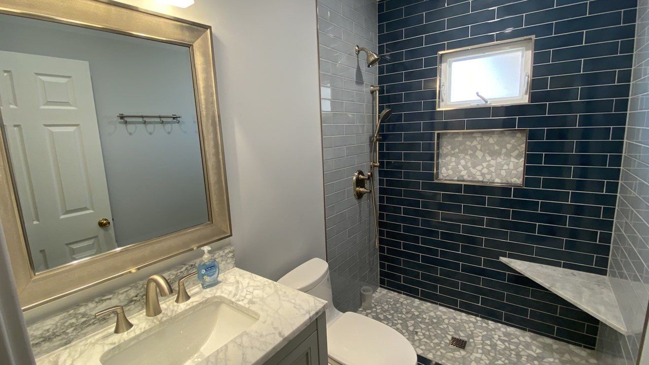 Remodeled bathroom with navy subway tile shower, framed mirror, and marble vanity