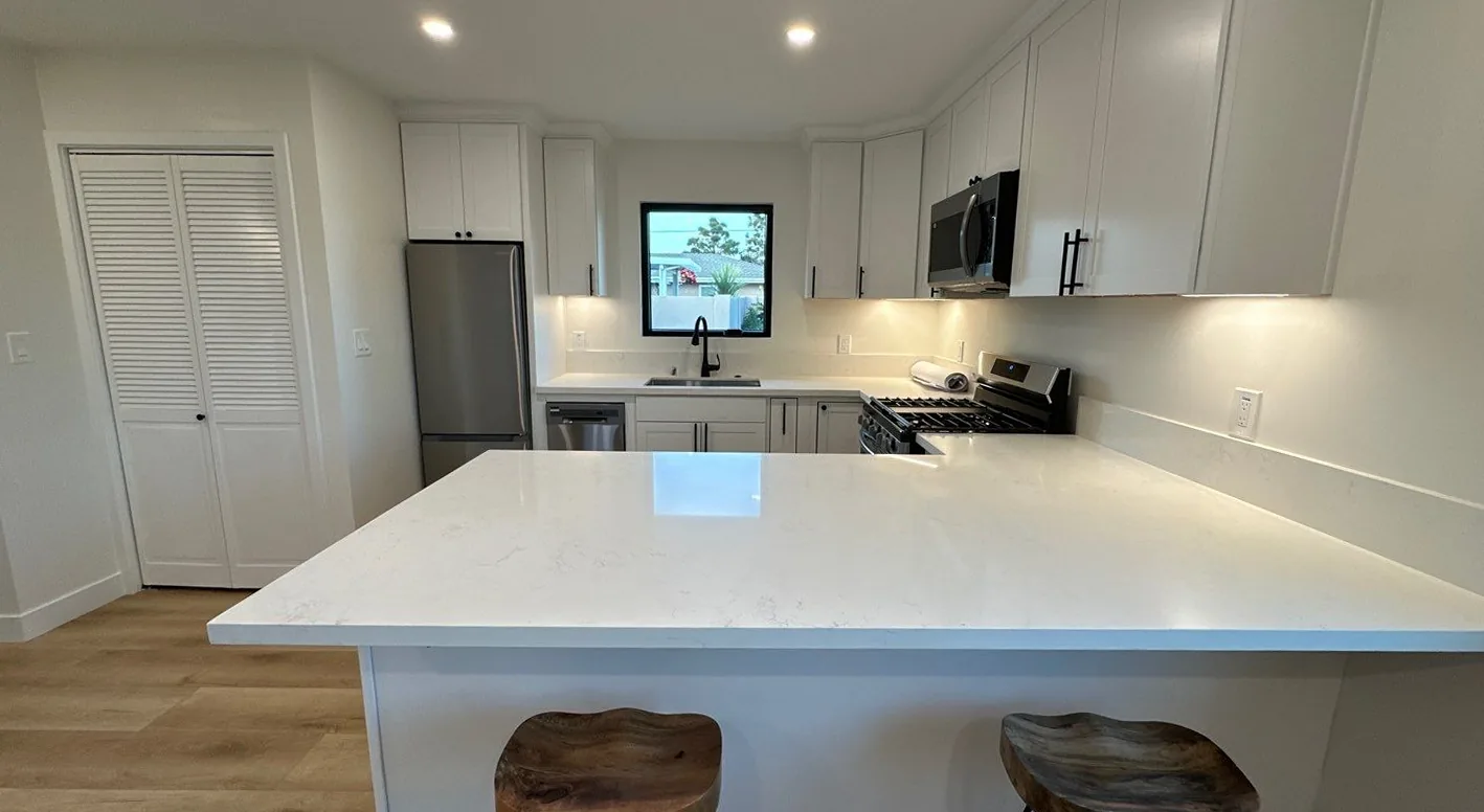 Bright South Bay kitchen remodel with white cabinetry, herringbone marble backsplash, lantern pendant lights, and an island with bar seating