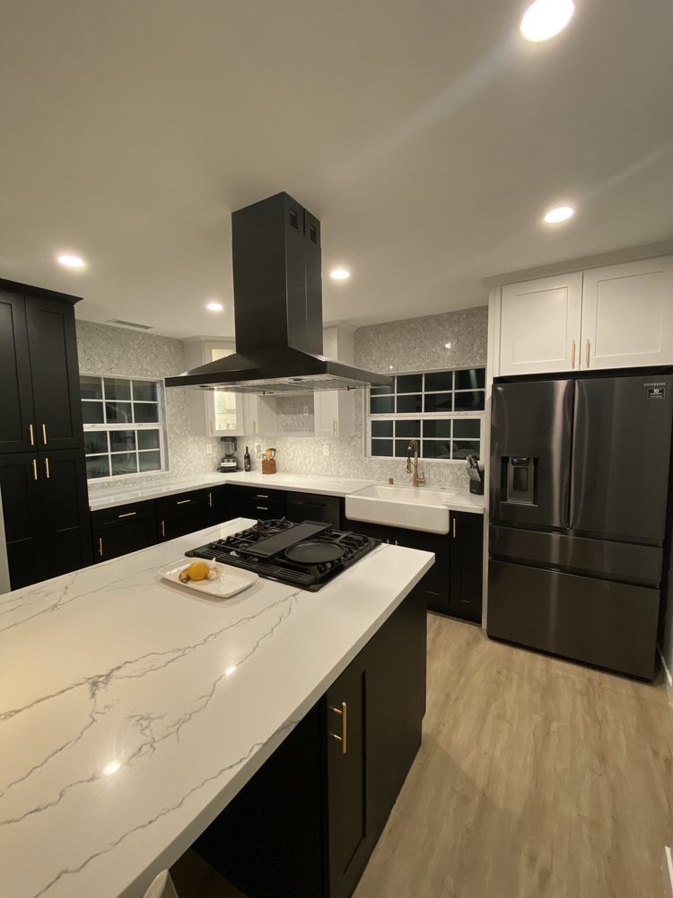 Same kitchen after remodel, with black cabinets, marble island, and new appliances