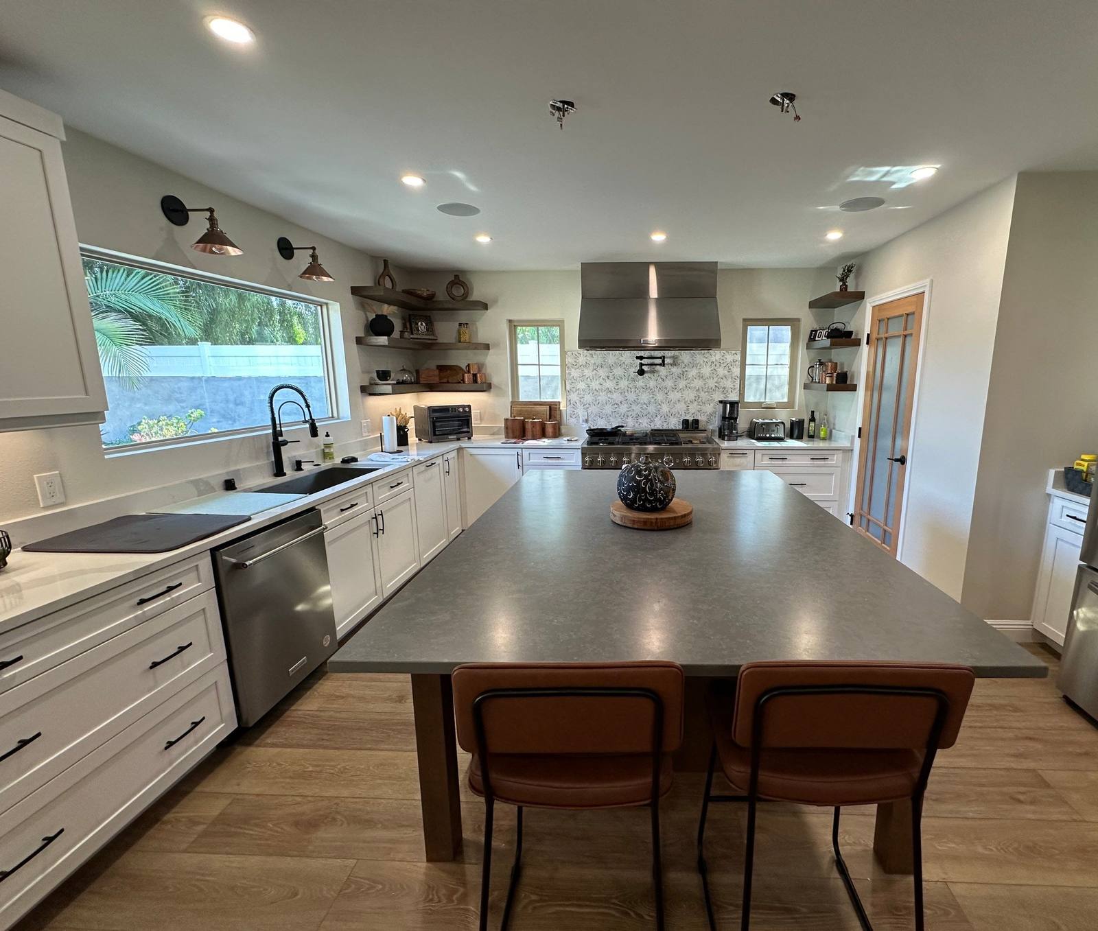 Open plan kitchen with white shaker cabinets, open wood shelving, and a large island with bar seating